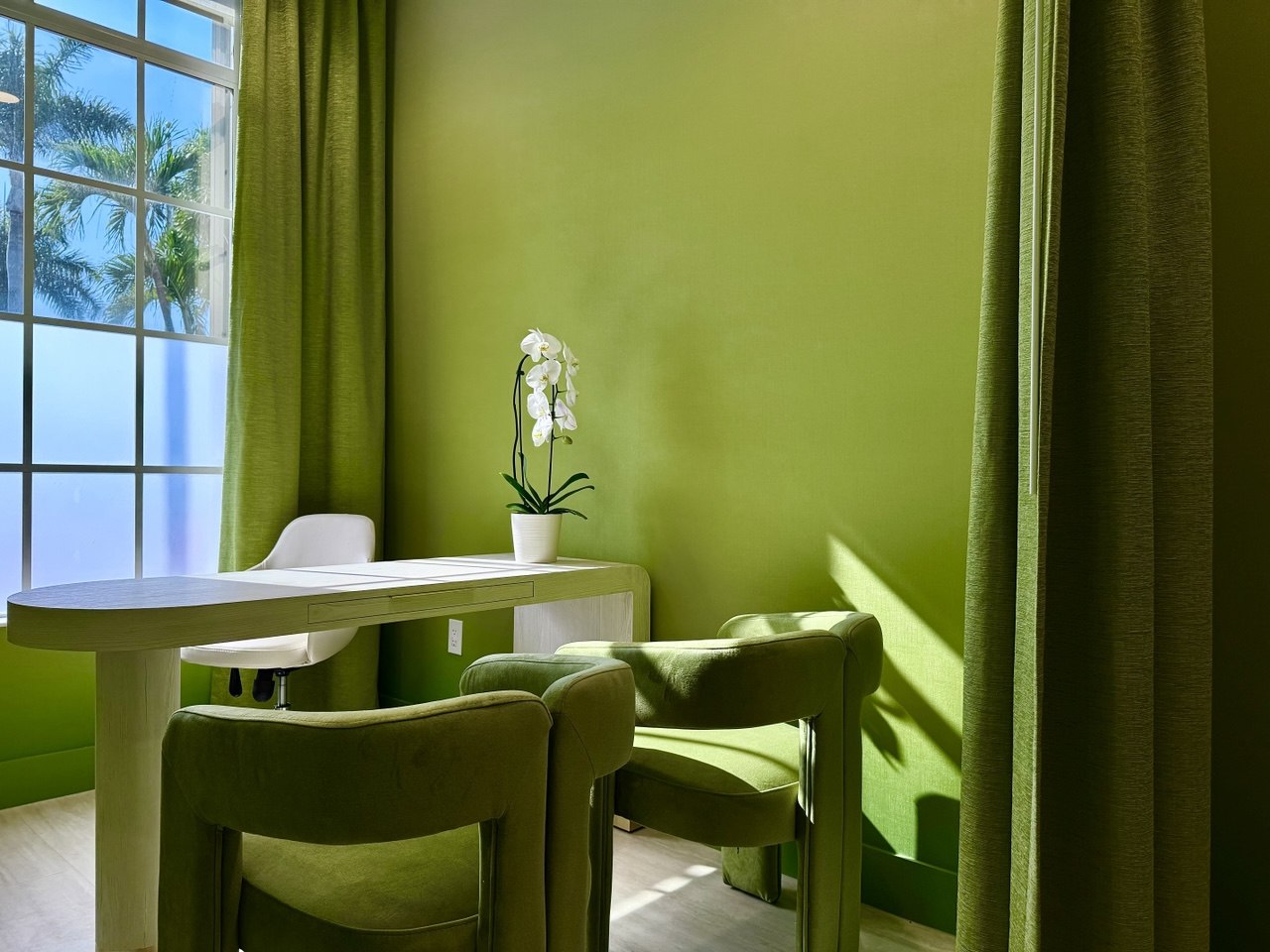 A sunlit consultation room washed in living green, a white orchid at its centre.