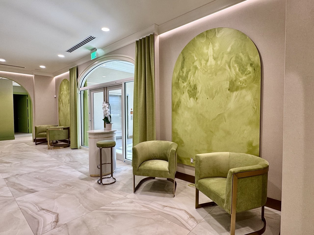 Hand-painted green arch murals above velvet armchairs.