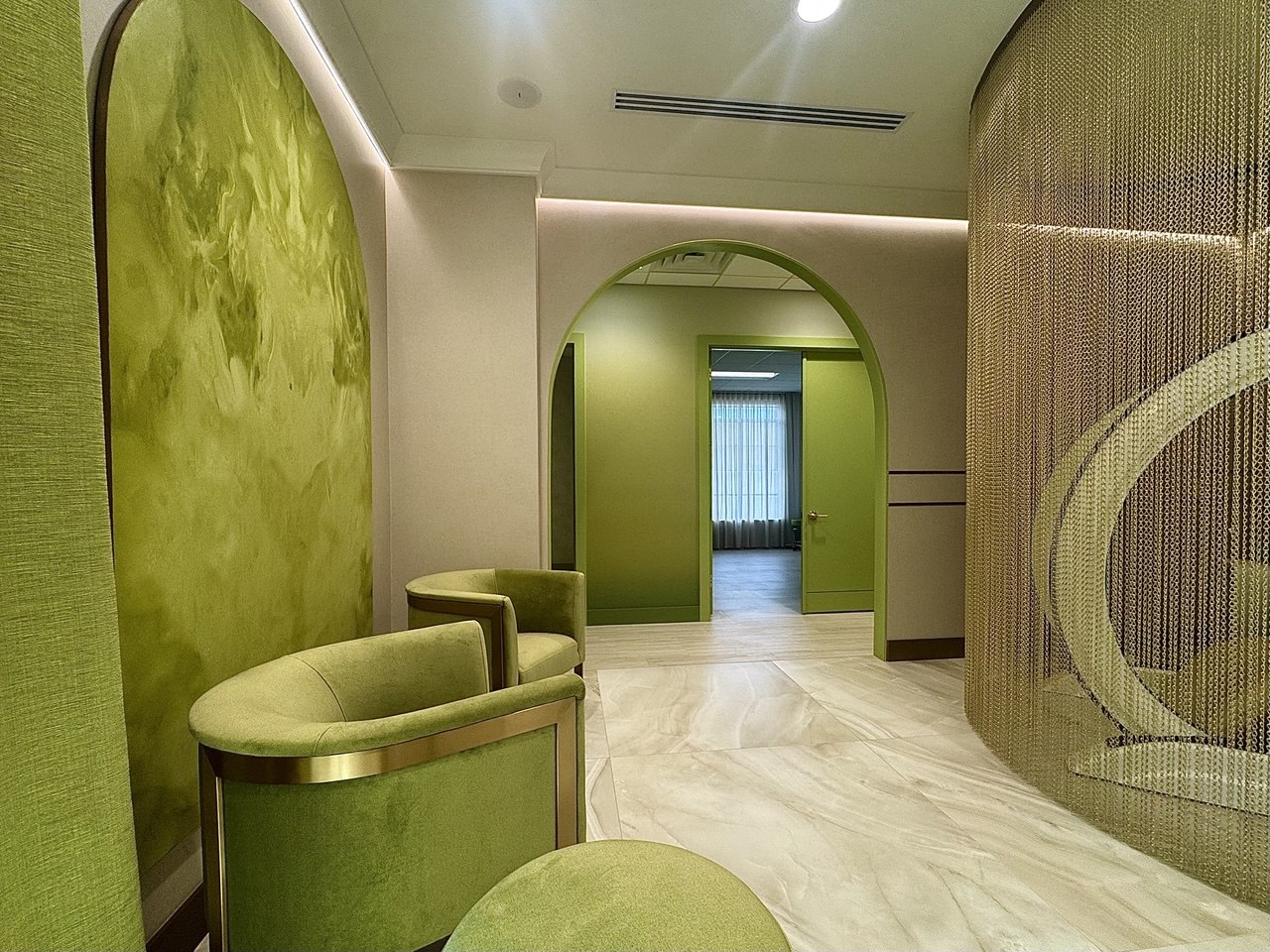 Green velvet chairs beside a champagne-gold chain curtain.